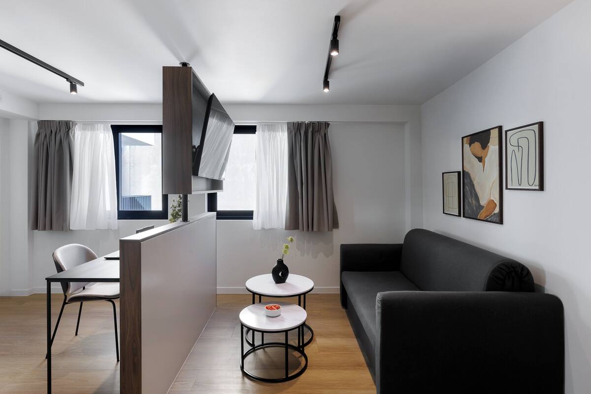 A modern living room with a black sofa, a dining table with chairs, and a small white table with a vase.