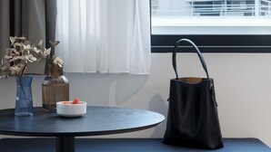 Ein modernes Zimmer mit einem runden Tisch, einer Bank, einer schwarzen Handtasche und einem Fenster mit Blick auf ein Wohngebäude.