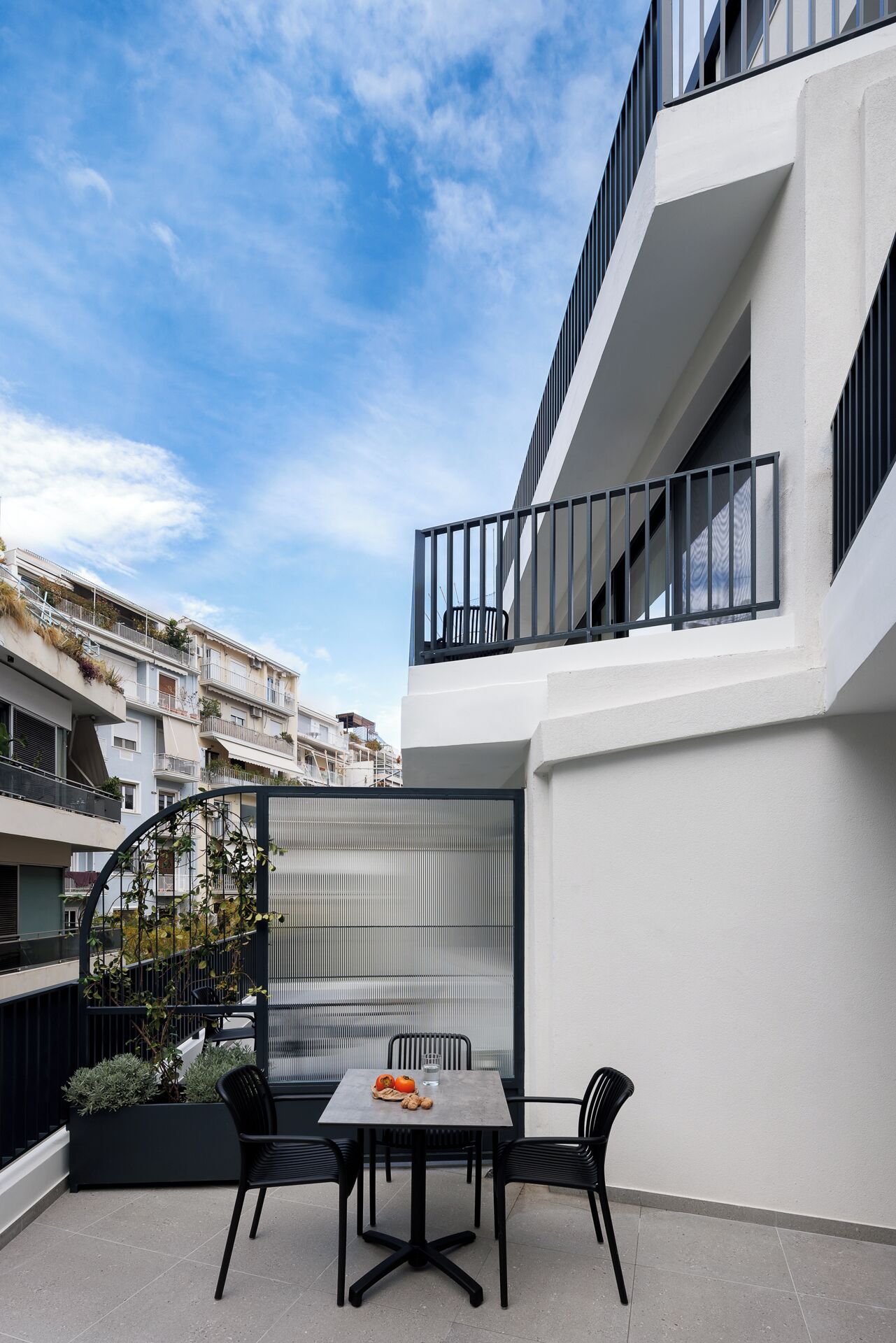 A modern outdoor patio with a table and chairs, a glass partition, and a view of adjacent buildings.