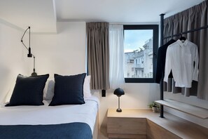 Une chambre d’hôtel moderne, équipée d’un lit, d’une table de chevet, d’une lampe et offrant une vue sur la ville par une fenêtre.