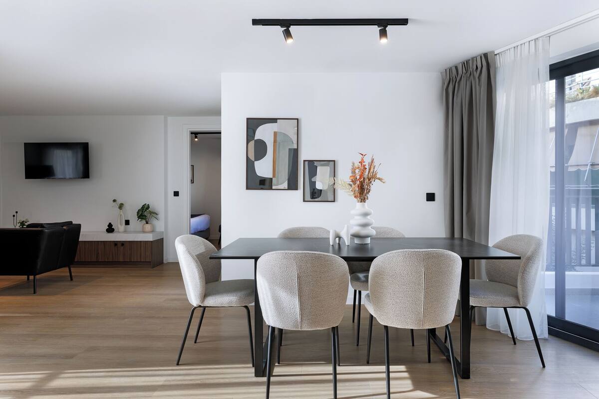 A modern dining area with a rectangular table, six chairs, and a vase with dried flowers.