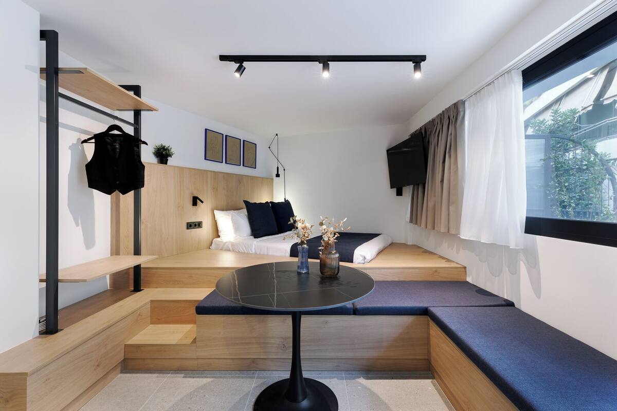 A modern, compact living space with a bed, seating area, and a small table.