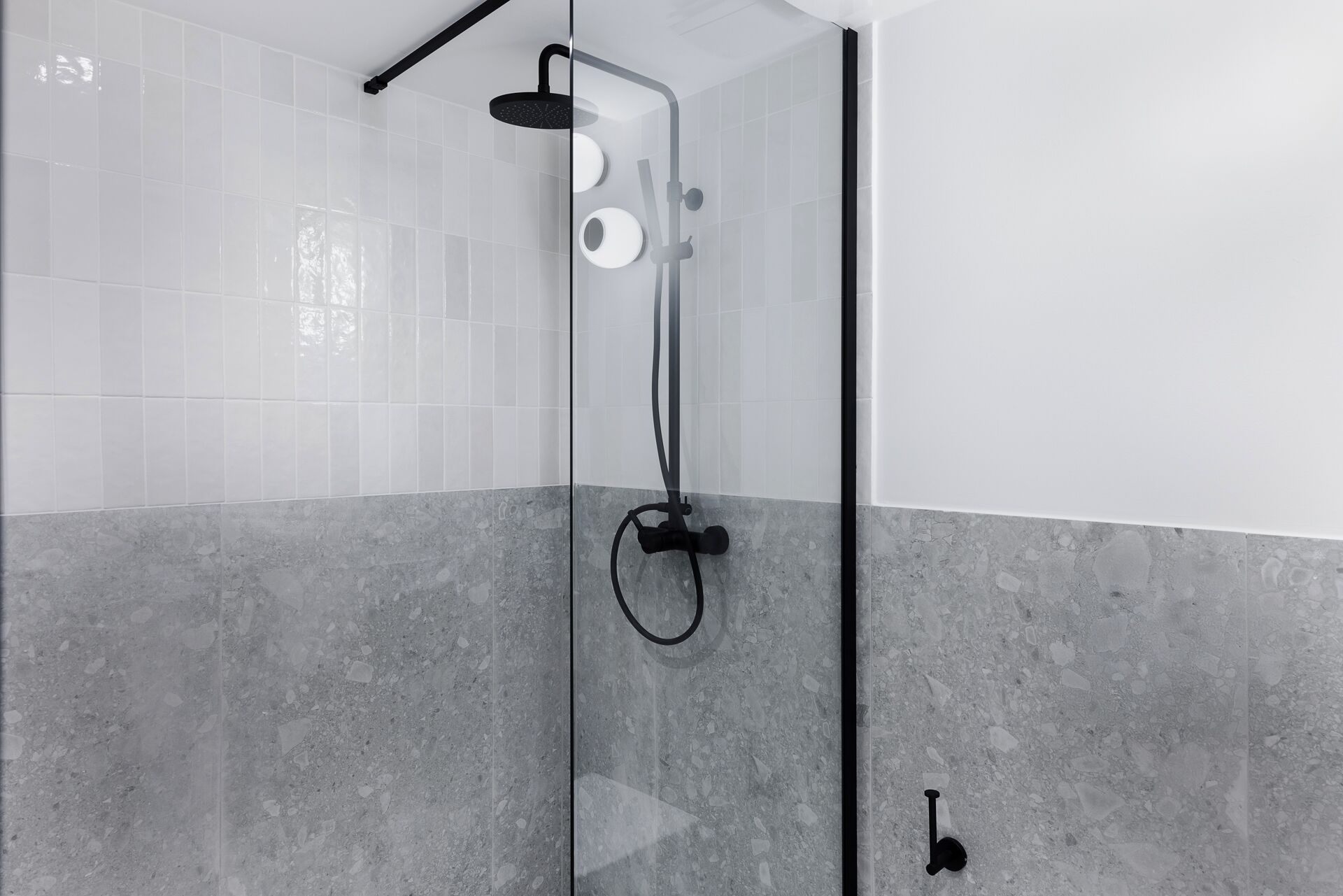 A modern shower with a glass enclosure, a handheld showerhead, and a wall-mounted control panel.