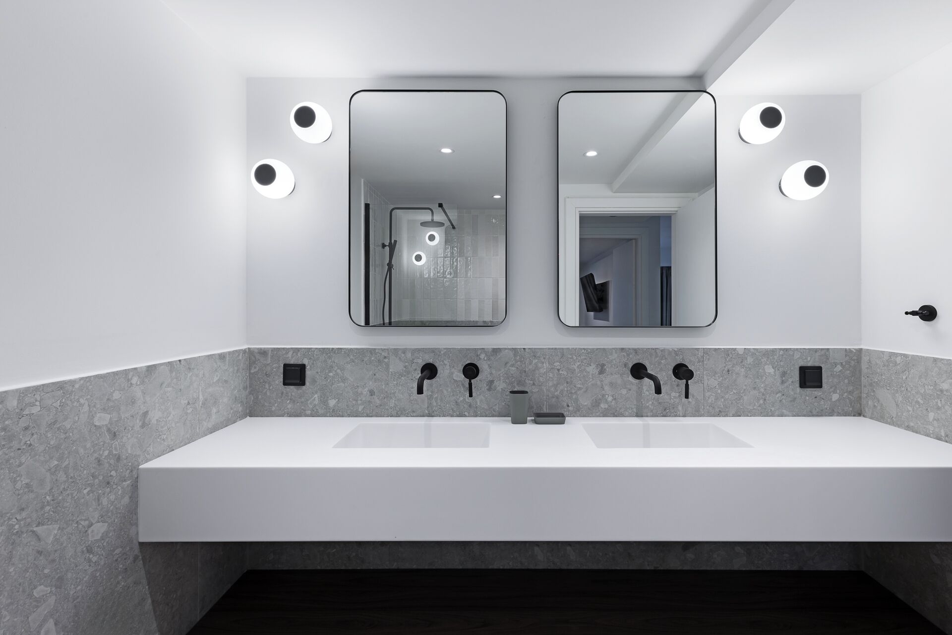 Un baño moderno con lavamanos doble, dos espejos montados en la pared y una ducha visible en el reflejo.