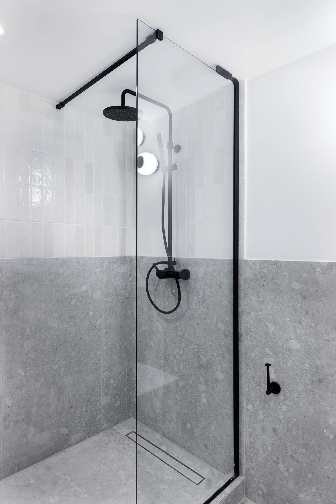 A modern shower enclosure with a glass door, a handheld showerhead, and a handheld shower attachment.