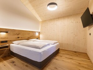 Una habitación con una cama, paredes de madera, una lámpara de techo y un televisor de pantalla plana montado en la pared.
