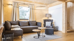 Una sala de estar acogedora con un sofá, un sillón y un otoman, una mesita redonda y una lámpara.