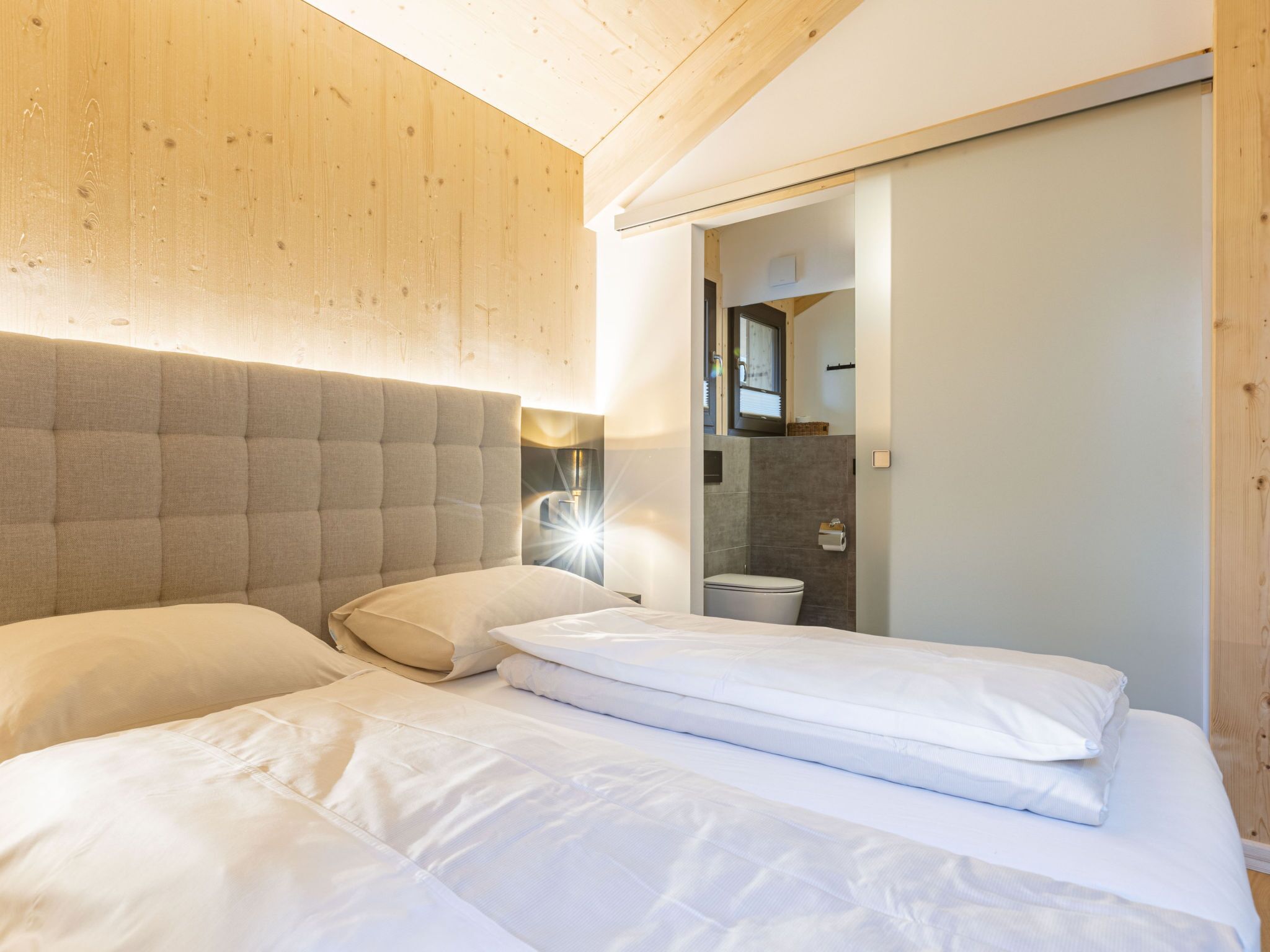 Quarto de hotel com uma cama grande, cabeceira e teto de madeira.