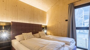 Un dormitorio con techo de madera, una cama con ropa blanca, dos lámparas de noche y un ventanal con cortinas.