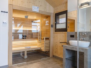 A modern bathroom with a wooden sauna, a glass-enclosed shower, and a sink with a mirror.