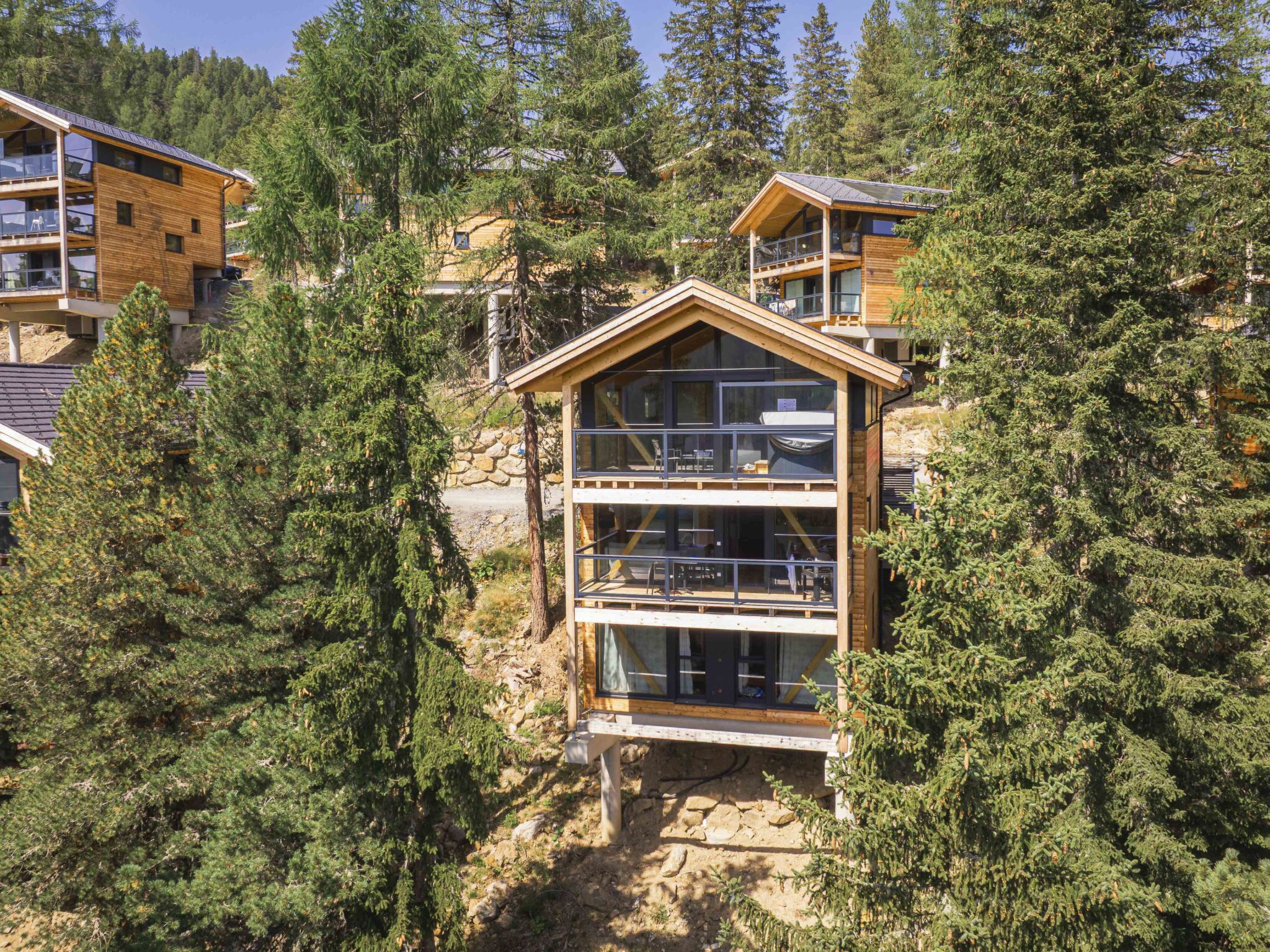 Une cabane en bois à plusieurs étages, dotée de grandes fenêtres et entourée d’une forêt dense.
