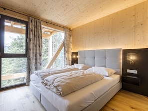 Une chambre avec un grand lit, des murs en bois et une vue sur les arbres par la fenêtre.