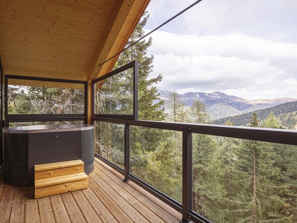 A wooden deck with a hot tub, overlooking a mountainous landscape.