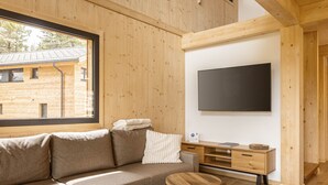 Un salon moderne avec un intérieur en bois, une grande fenêtre, un canapé, un téléviseur à écran plat et une petite table en bois.