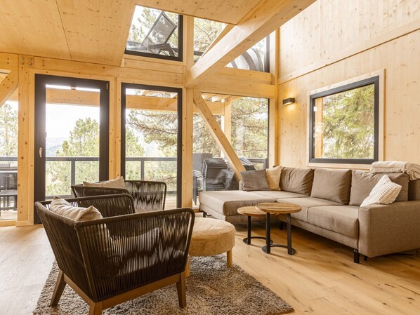 A spacious living room with a wooden interior, large windows, and a sofa set.