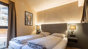 A bedroom with two beds, wooden walls, a framed picture, bedside lamps, and a window with curtains.