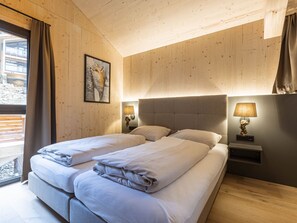 Une chambre avec deux lits, des murs en bois, un tableau encadré, des lampes de chevet et une fenêtre avec des rideaux.
