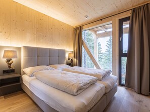 A double bed in a room with wooden walls and a sloped ceiling, a window with curtains, and two bedside lamps.