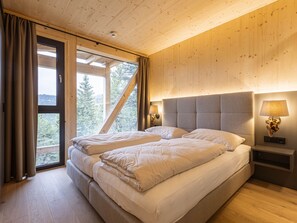 Een slaapkamer met een groot bed, twee nachtkastjes, een raam met gordijnen en uitzicht op bomen.
