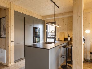 Een moderne keuken met een centraal eiland, krukken, hanglampen en houten keukenkastjes.