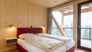 A bedroom with a wooden ceiling, a red headboard, a bed with white linens, a nightstand, and a window with a view of trees.
