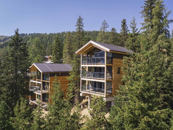 Two multi-story wooden cabins with balconies, surrounded by dense forest.
