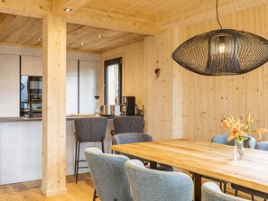 A modern kitchen with a wooden ceiling, a dining area with a wooden table and grey chairs, and a hanging light fixture.
