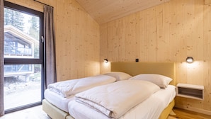 A room with wooden walls and a large window, featuring two beds with white bedding and a nightstand.