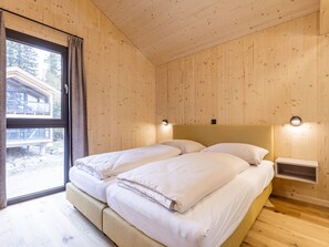 A room with wooden walls and a large window, featuring two beds with white bedding and a nightstand.