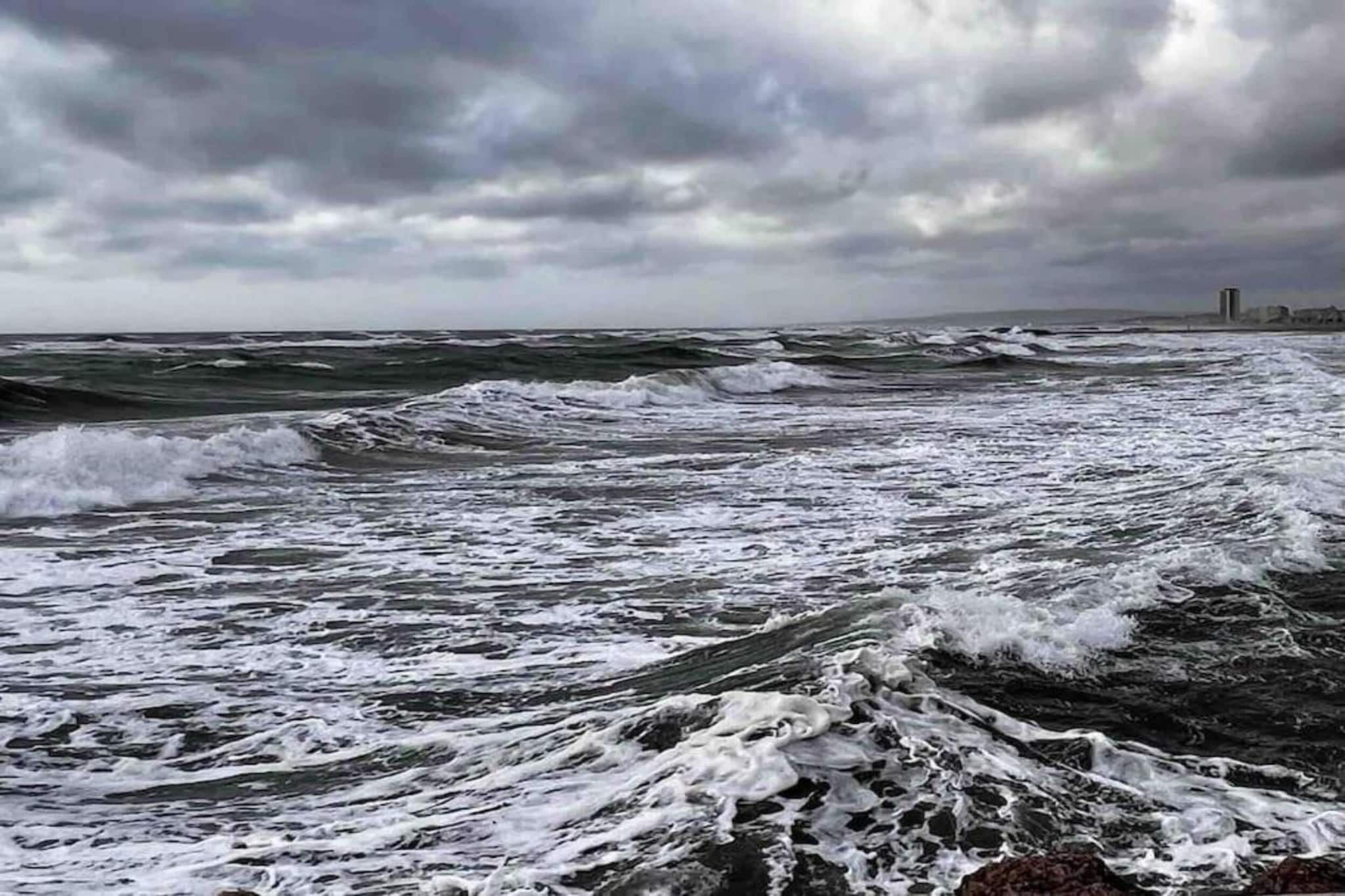Paesaggio costiero con onde spumeggianti e cielo nuvoloso.