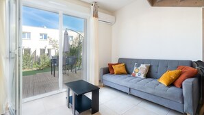 Un salon moderne avec un canapé gris, une table basse noire et une porte-fenêtre coulissante donnant sur une terrasse.