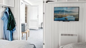 A bedroom with a bed, a TV mounted on the wall, a coat rack, and a door leading to another room.