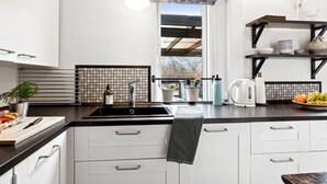 A modern kitchen with white cabinets, a black countertop, a hanging light fixture, a window with a view, and a shelf with kitchenware.