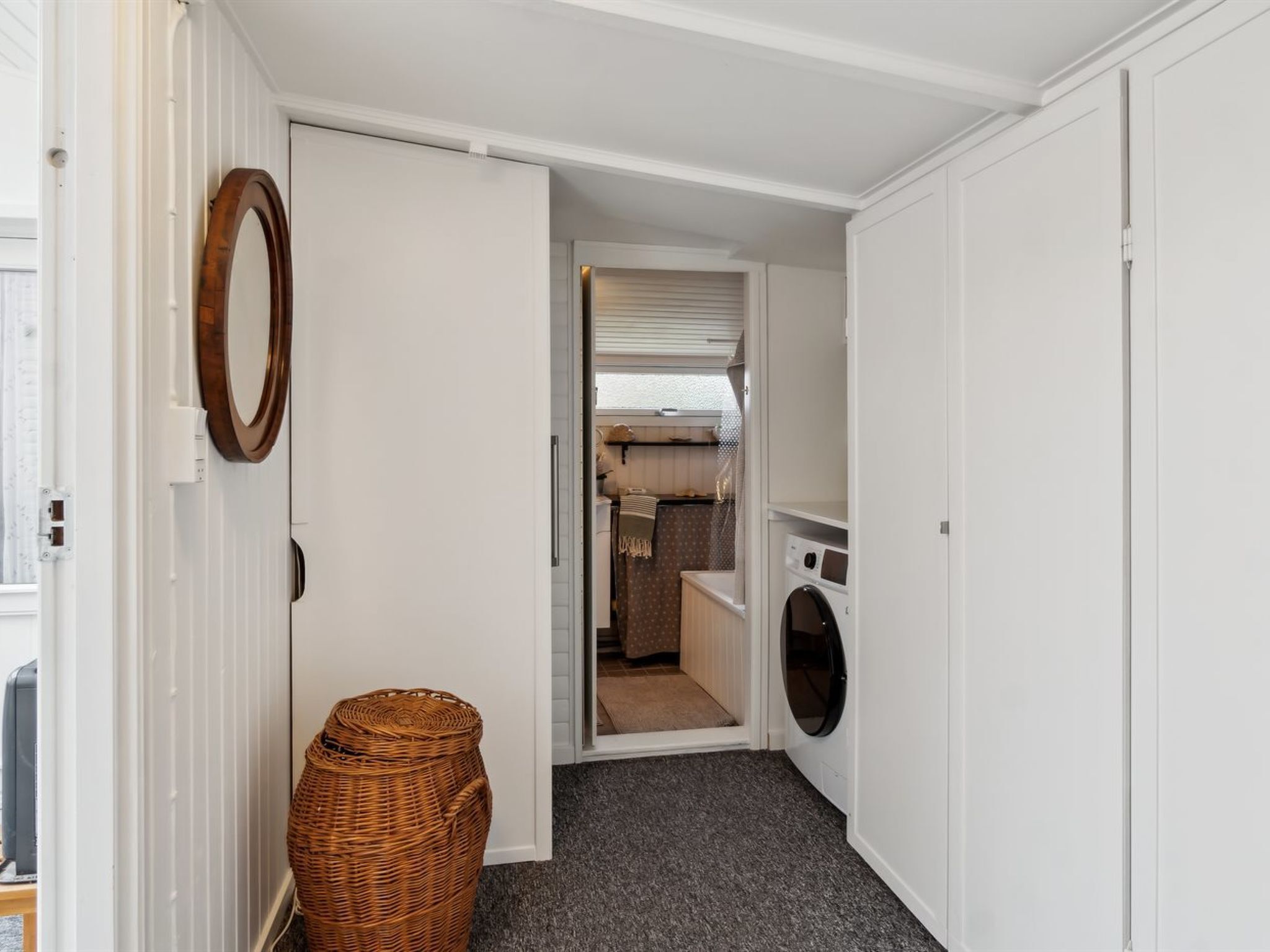 A laundry room with a washing machine, a wicker basket, and a door leading to a kitchen area.