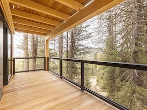 Une terrasse en bois dotée d’une rambarde, qui offre une vue sur une zone boisée.