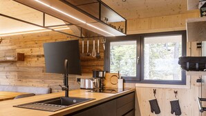 A modern kitchen with a wooden interior, a large window, and various kitchen utensils. - 02_NTH019_Sup Chalet mit Sauna und Hot Tub 2 Etage by Interhome (Turracher Höhe)