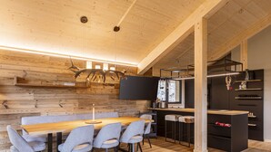A modern kitchen with a wooden wall, a dining table with chairs, and a built-in stove. - 02_NTH019_Sup Chalet mit Sauna und Hot Tub 2 Etage by Interhome (Turracher Höhe)