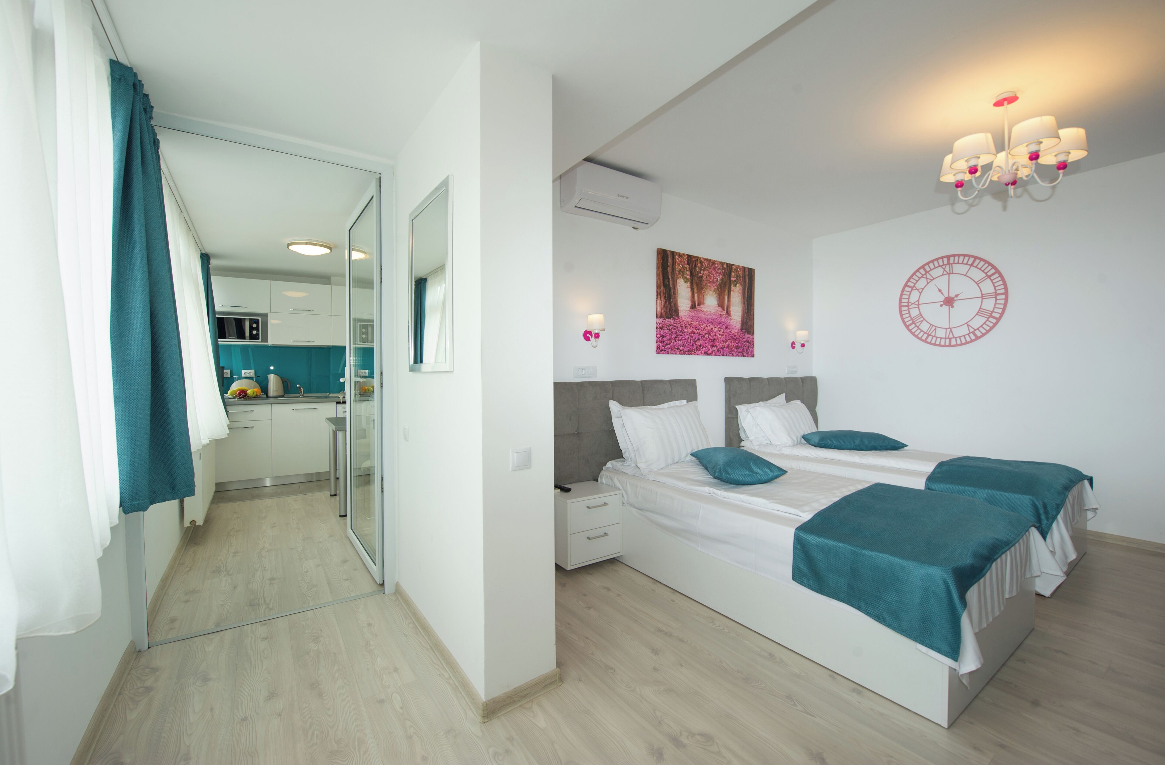 A modern bedroom with a large bed, a bedside table, a nightstand, a wall-mounted clock, and a window with curtains.
