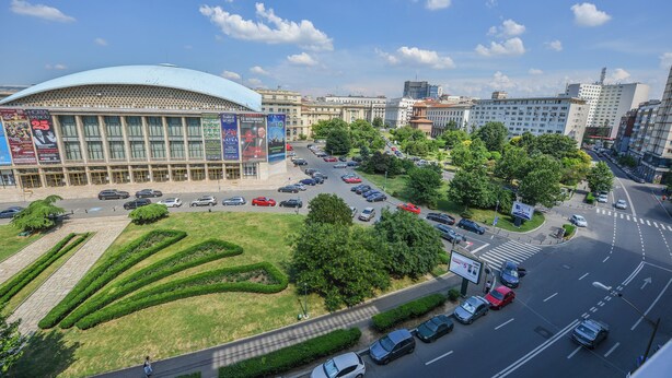 Un grand bâtiment doté d’un toit bleu, entouré d’un parking et de verdure.