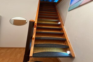 A wooden staircase with carpeted steps and a handrail, leading to a landing with a mirror and a painting on the wall.