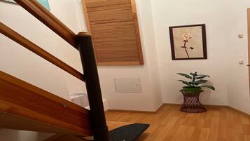 Eine Holztreppe mit Handlauf, ein Holzboden, ein an der Wand befestigtes Fenster, ein gerahmtes Rosenbild und ein Blumentopf.
