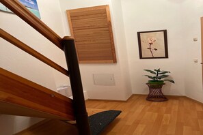 A wooden staircase with a handrail, a wooden floor, a wall-mounted window, a framed picture of a rose, and a potted plant.
