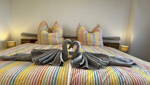 A bed with striped bedding, two pillows, and towels arranged in a heart shape. - Airy City Apartment in Zwickau (Zwickau)