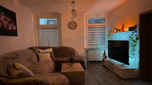 A cozy living room with a brown sofa, a wooden coffee table, and a fireplace with a Christmas tree. - Airy City Apartment in Zwickau (Zwickau)