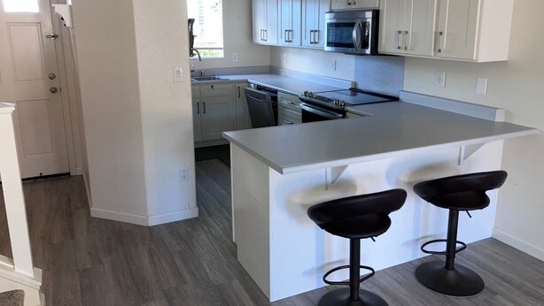 A modern kitchen with white cabinets, a stainless steel microwave, and a large island with two bar stools. - Charming 3-bedroom townhome with AC, WiFi in serene Ewa Beach (Ewa Beach)