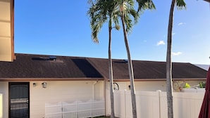 A house with a white exterior, a dark roof, a white fence, and a paved driveway. - Charming 3-bedroom townhome with AC, WiFi in serene Ewa Beach (Ewa Beach)