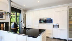 A modern kitchen with white cabinetry, a black countertop, and stainless steel appliances. - Magnificent villa with indoor pool and prime lake view location (Brione sopra Minusio)