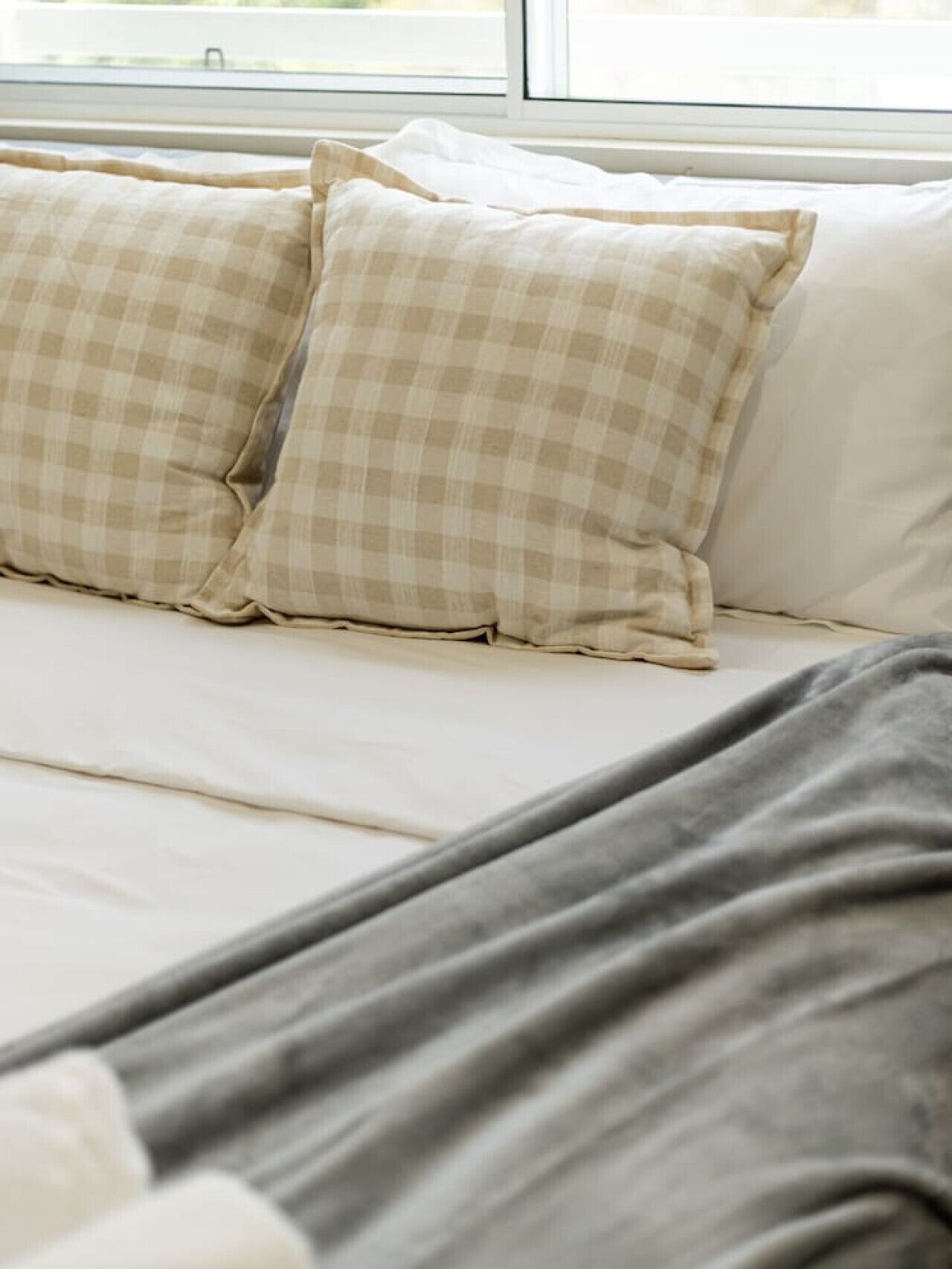 A bed with checkered pillows and a grey blanket.