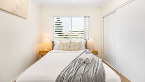 A hotel room with a large bed, two bedside tables with lamps, a window with blinds, and a ceiling fan. - Walk to everything! Modern 2Beds Apt w/ EasyAccess (Springwood)