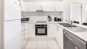 A modern kitchen with white cabinets, a built-in oven, a dishwasher, and a stainless steel sink. - Walk to everything! Modern 2Beds Apt w/ EasyAccess (Springwood)